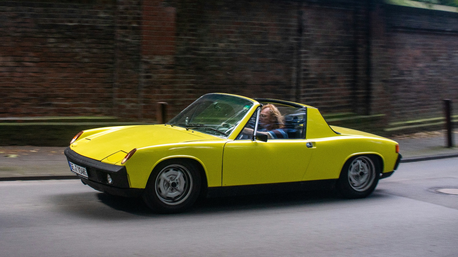 A yellow convertible car driving down a street