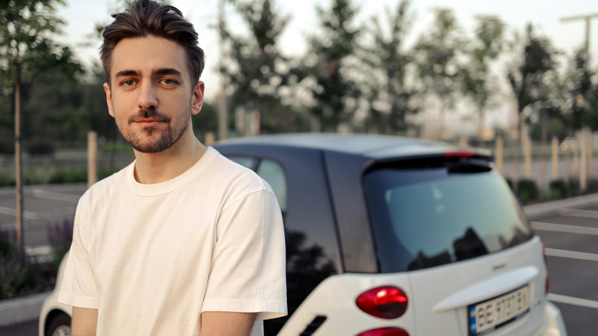 man in white crew neck t-shirt standing beside white car during daytime