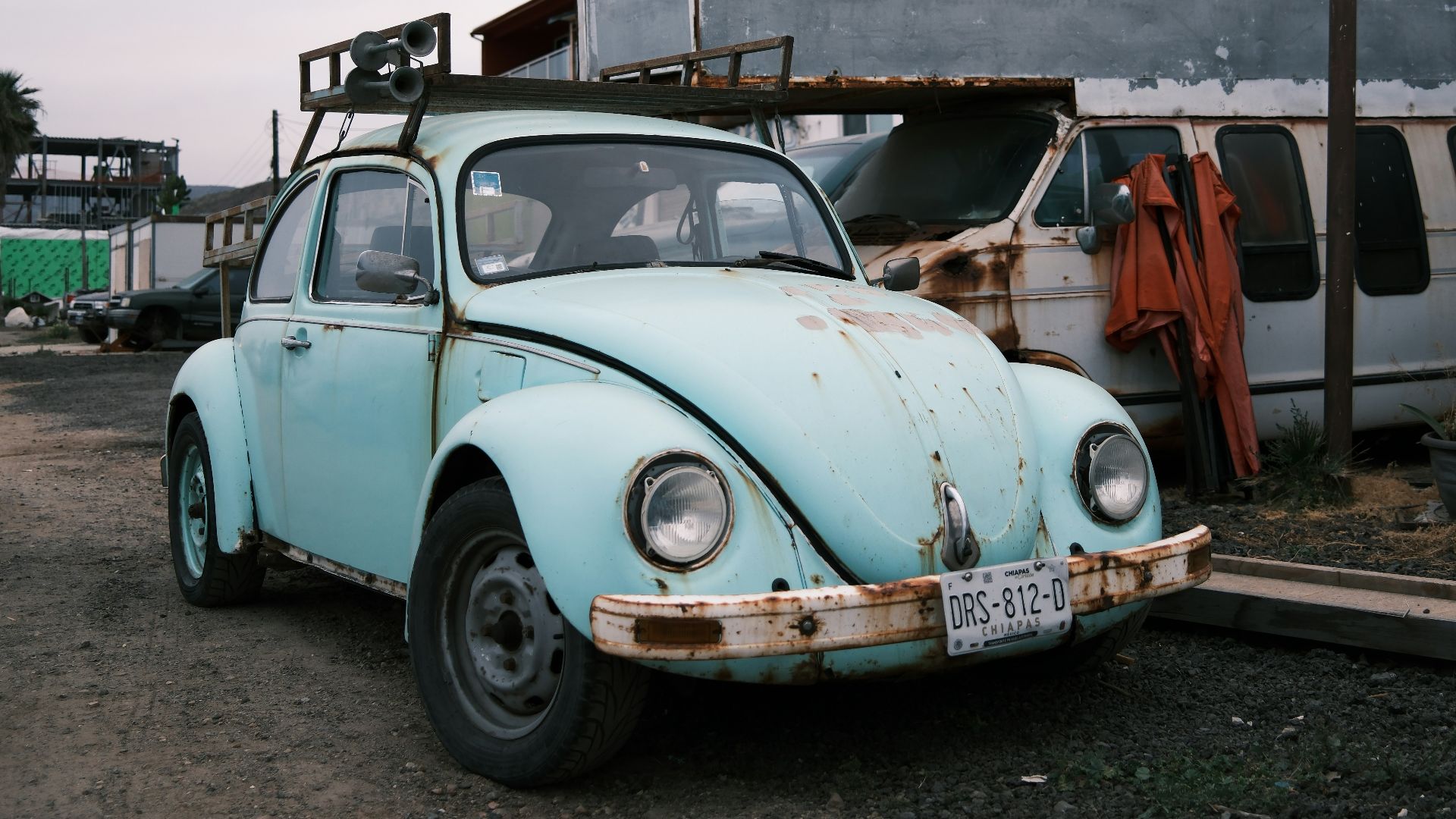 A weathered blue car is parked near a building.