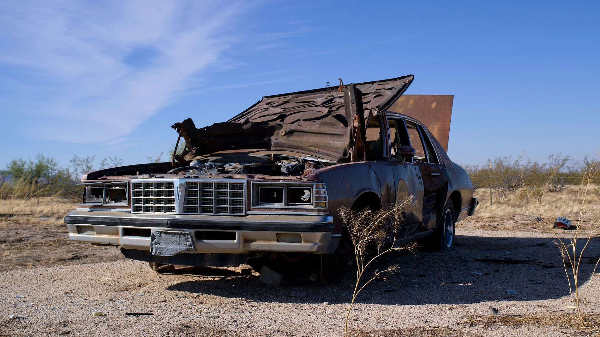 A wrecked car sits abandoned in a dry, desolate landscape.