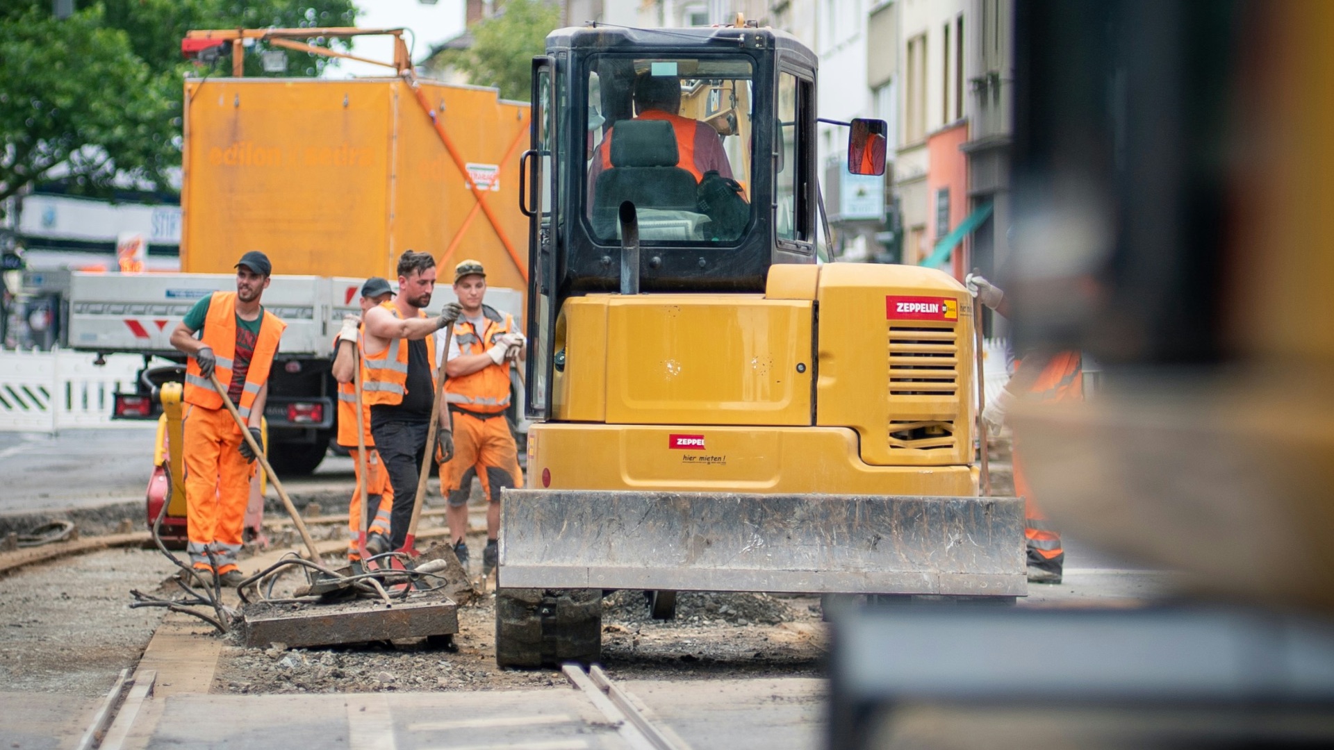 man in orange jacket standing beside yellow truck during daytime