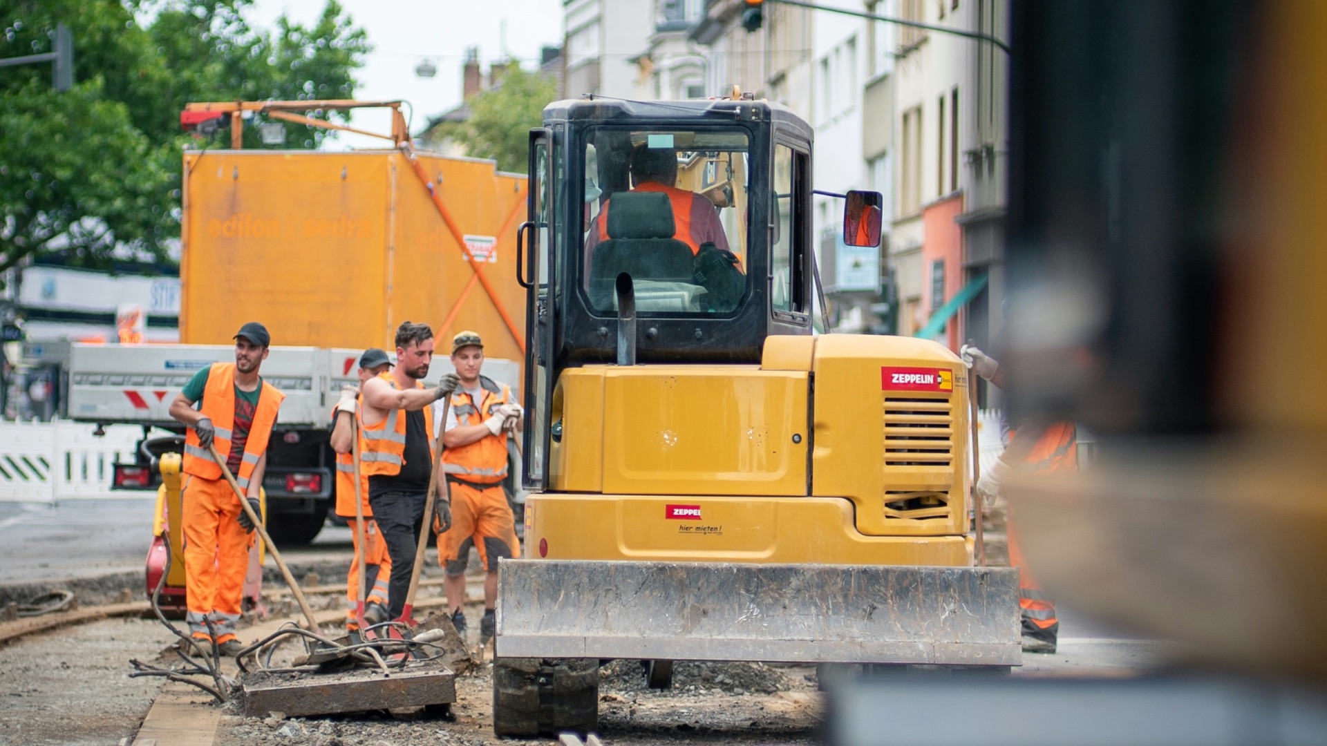 man in orange jacket standing beside yellow truck during daytime