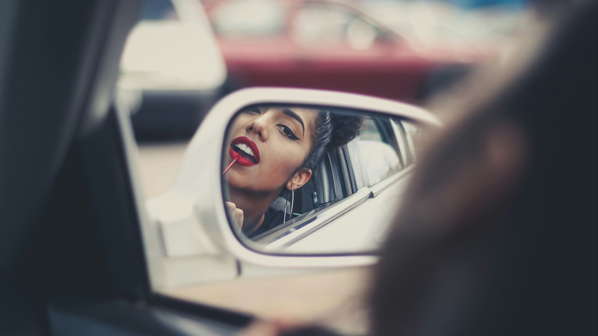 woman putting liquid lipstick on her lips while looking at vehicle's mirror during daytime