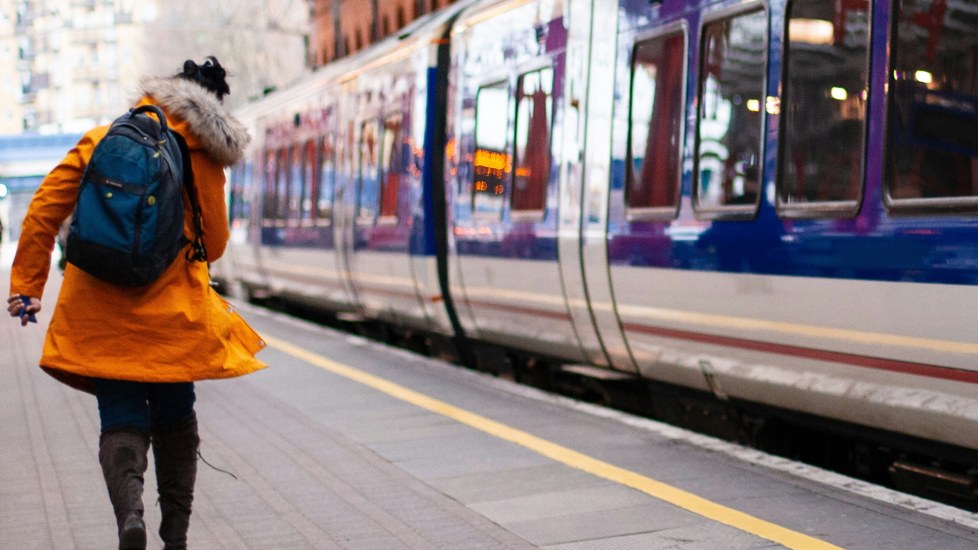 woman in orange coat walking beside train at the station
