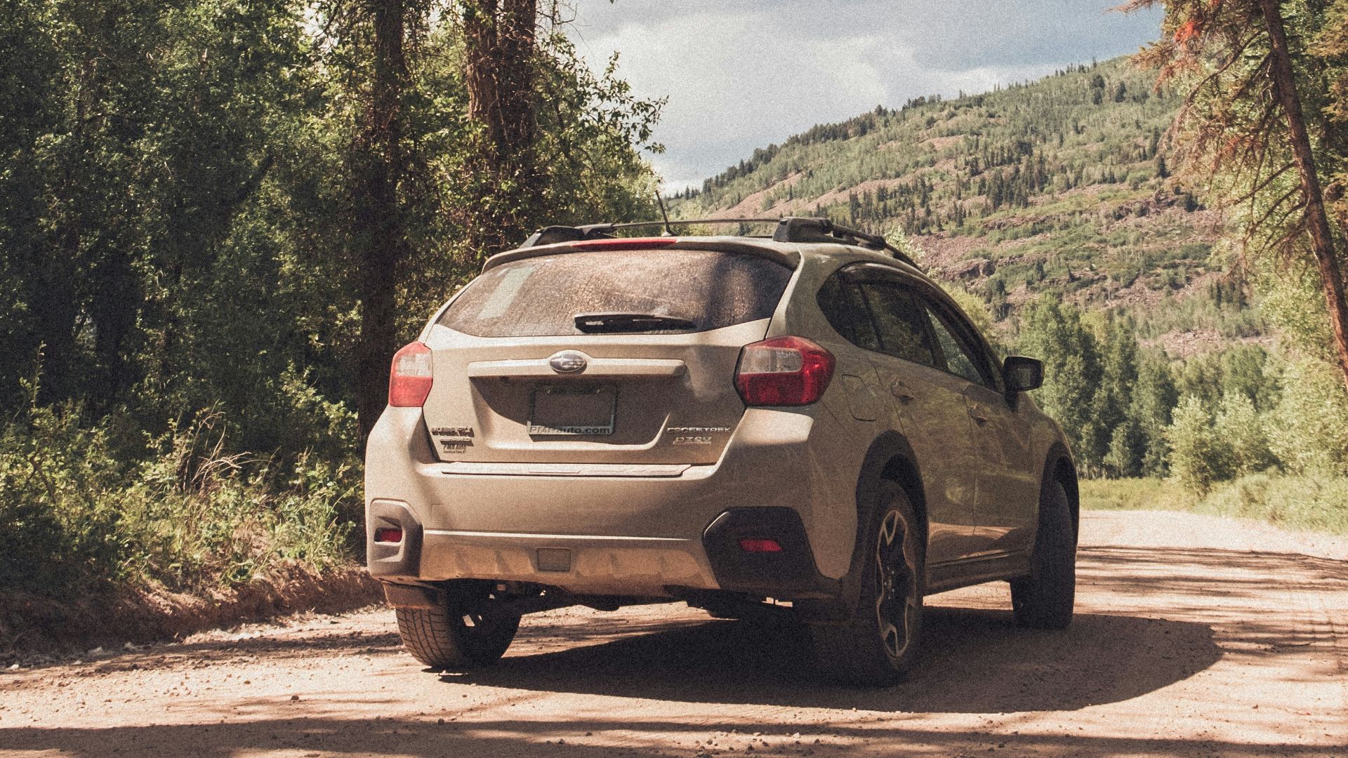 a white car driving down a dirt road next to a forest