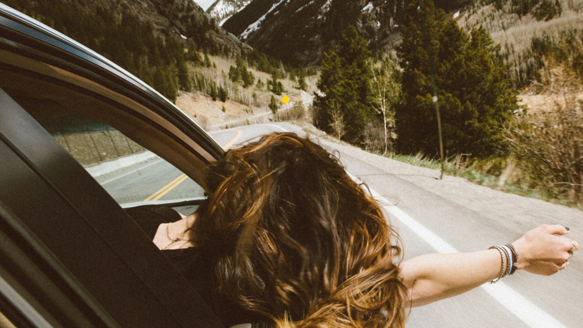 woman riding on vehicle putting her head and right arm outside the window while travelling the road