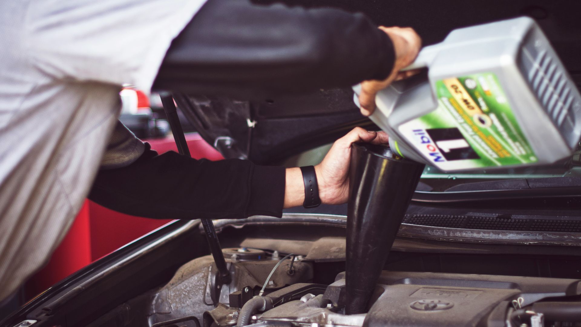 man refilling motor oil on car engine bay