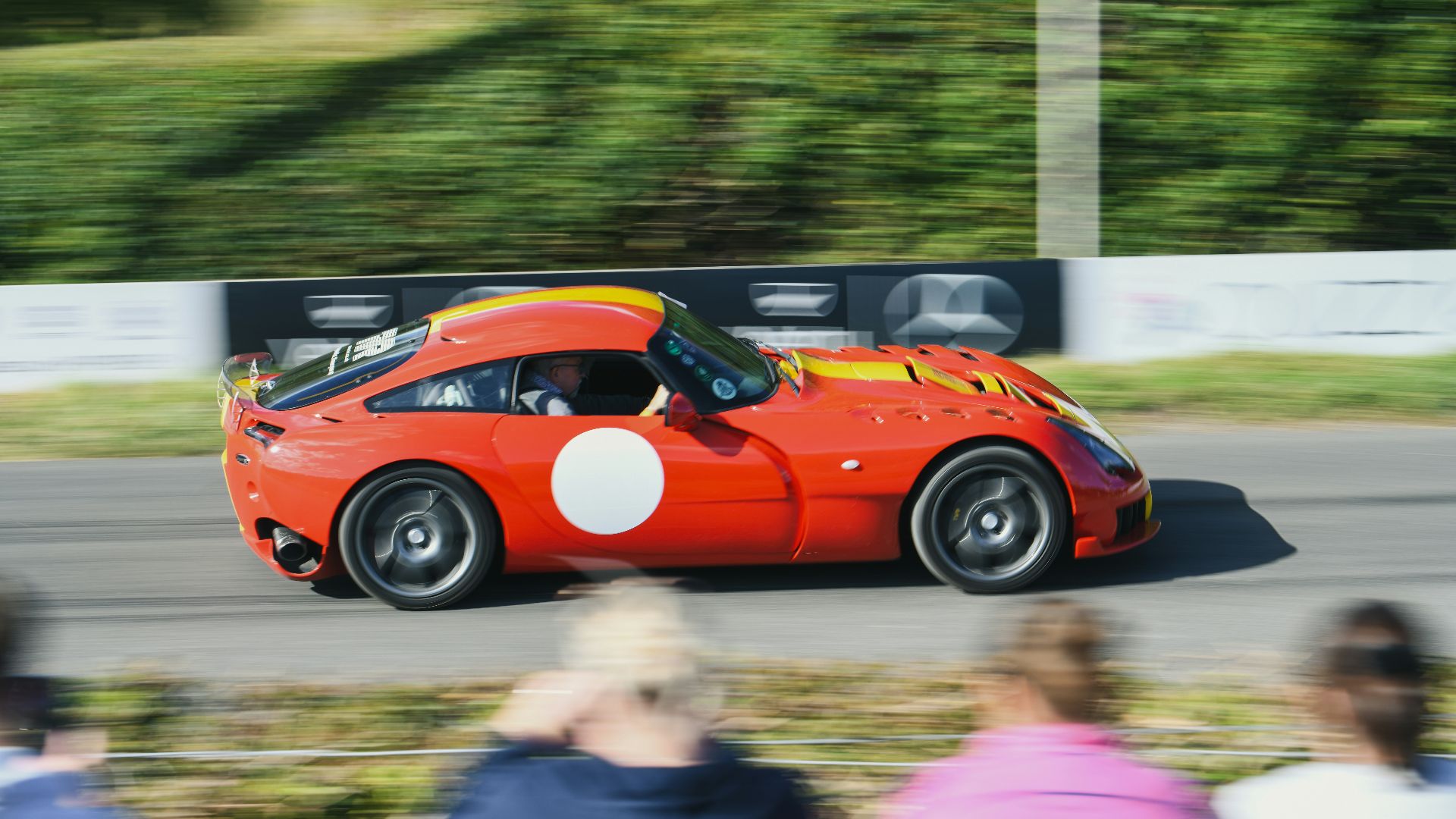 Red sports car racing on a track with spectators.