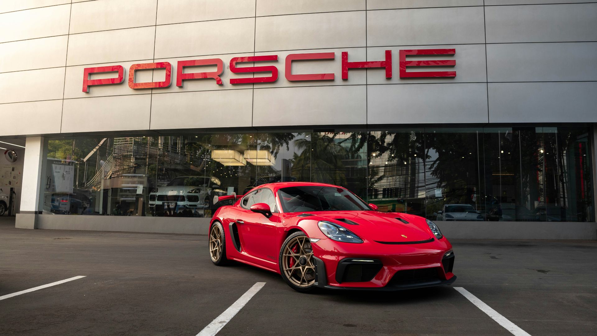 a red sports car parked in front of a porsche dealership