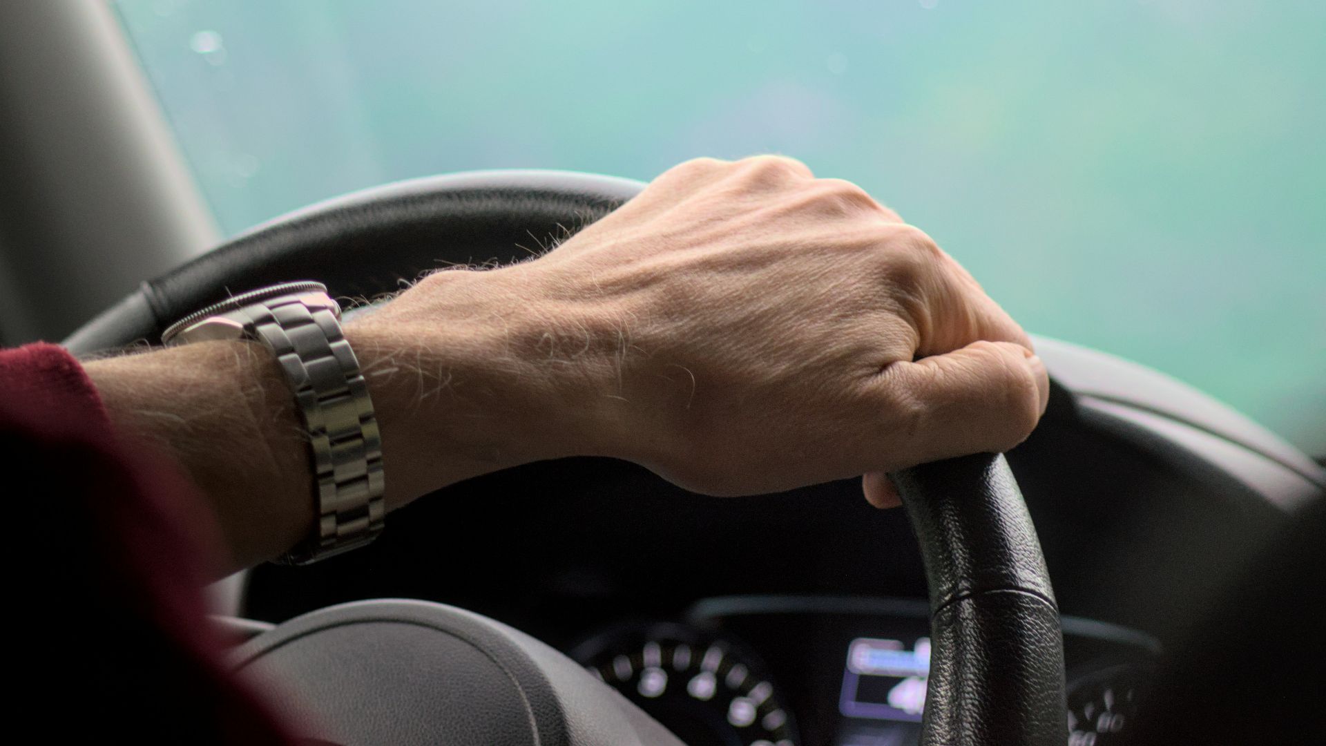 Hand gripping a steering wheel while driving.