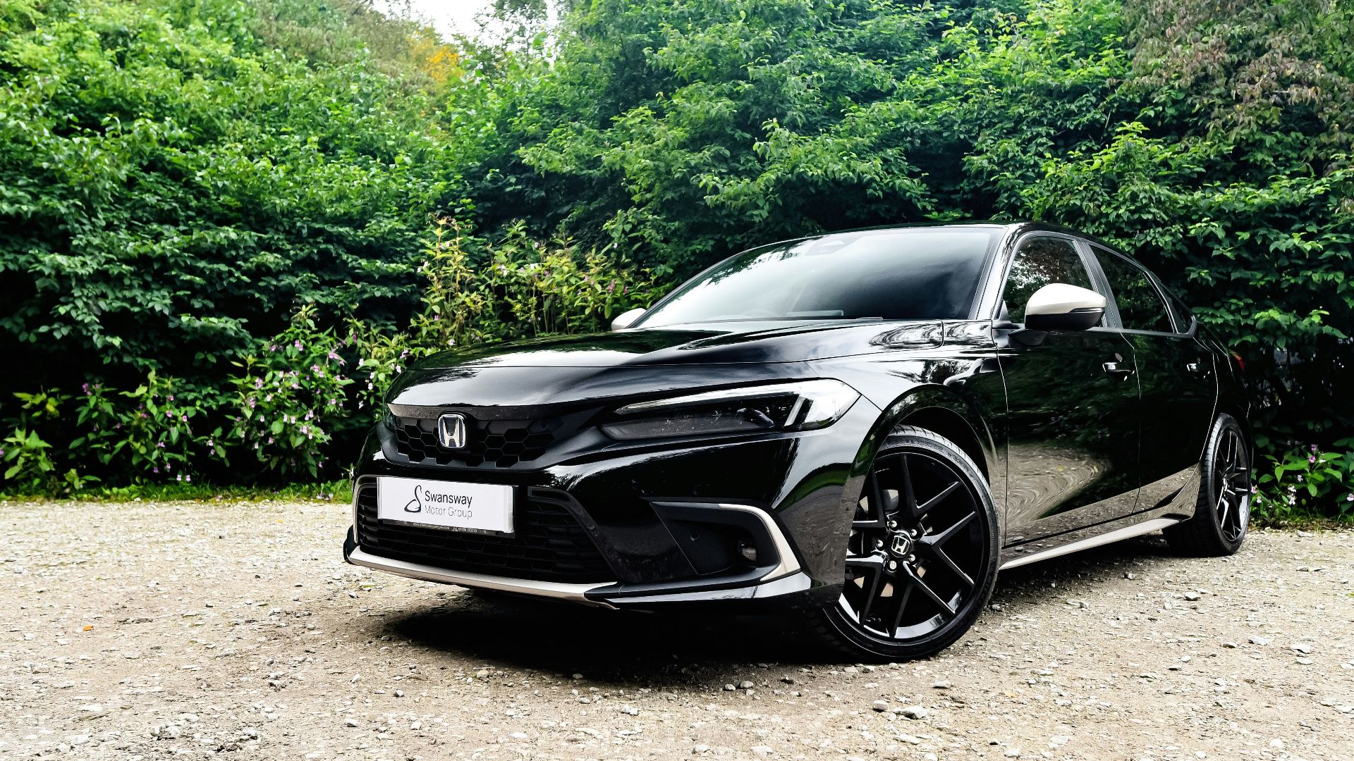 a black car parked on a gravel road with trees in the background