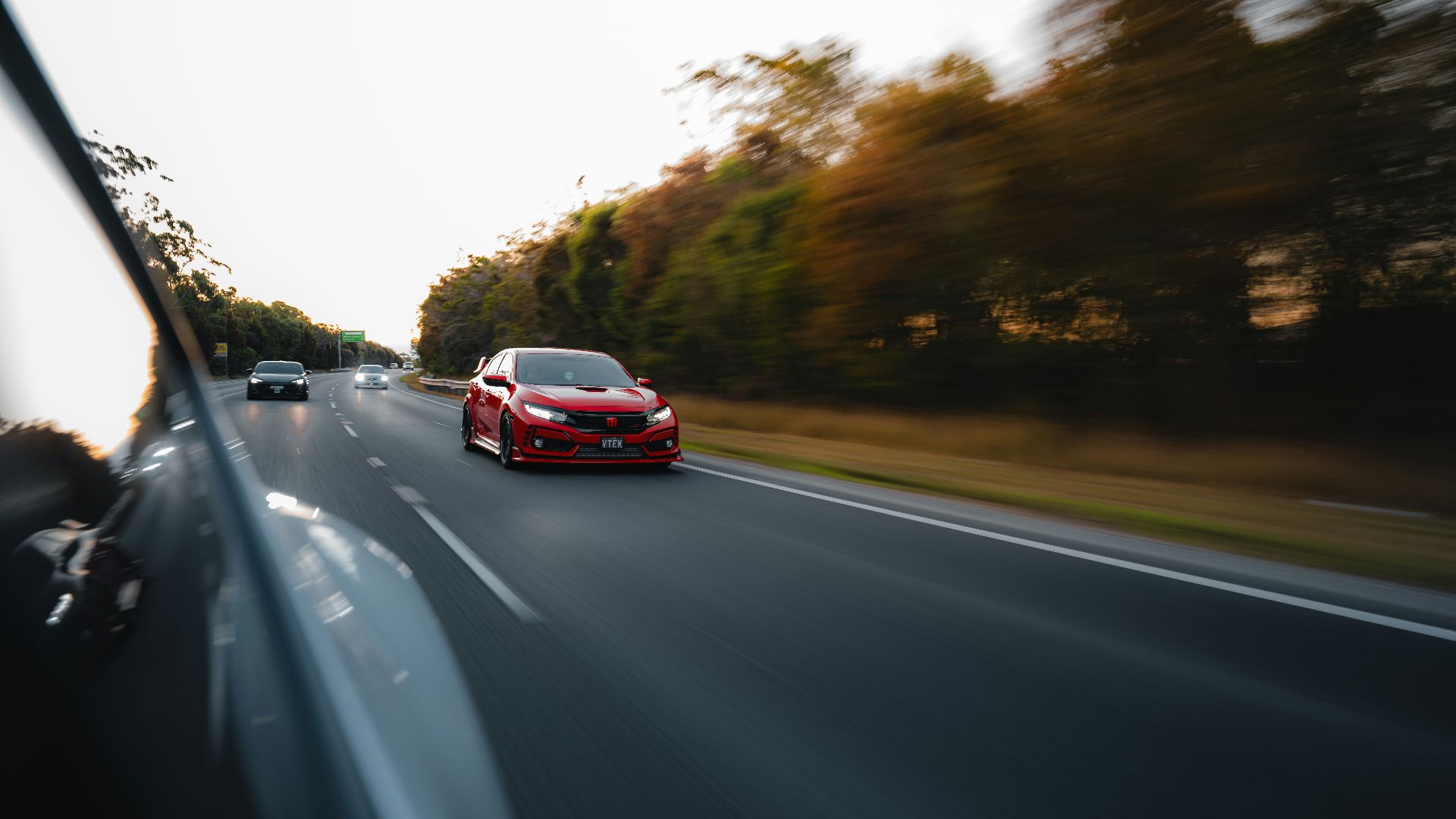 a red car driving down a road next to a forest