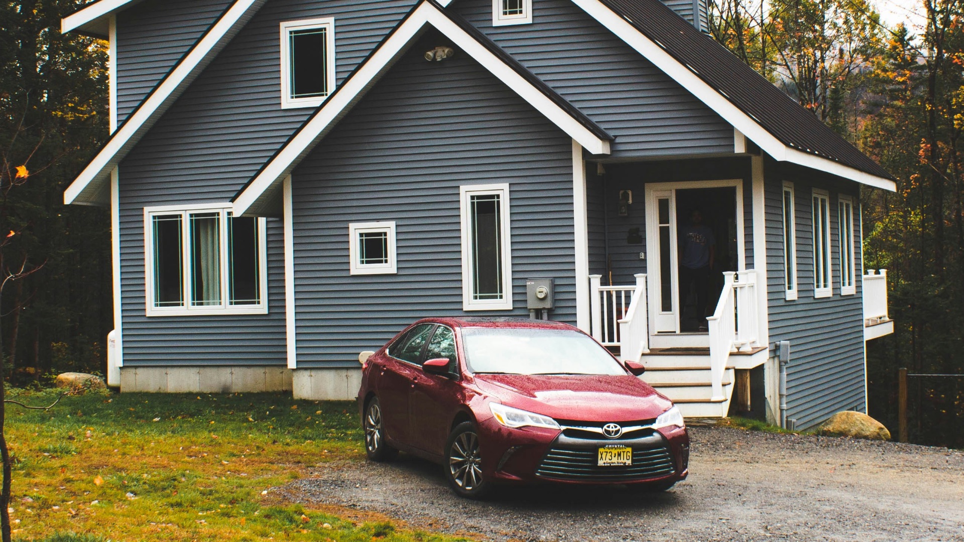red car parked beside white wooden house