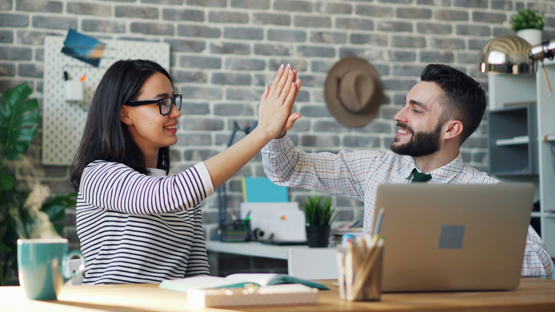 a man and a woman high fiving each other in front of a laptop