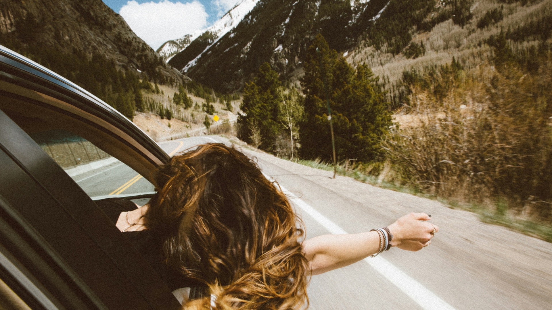 woman riding on vehicle putting her head and right arm outside the window while travelling the road