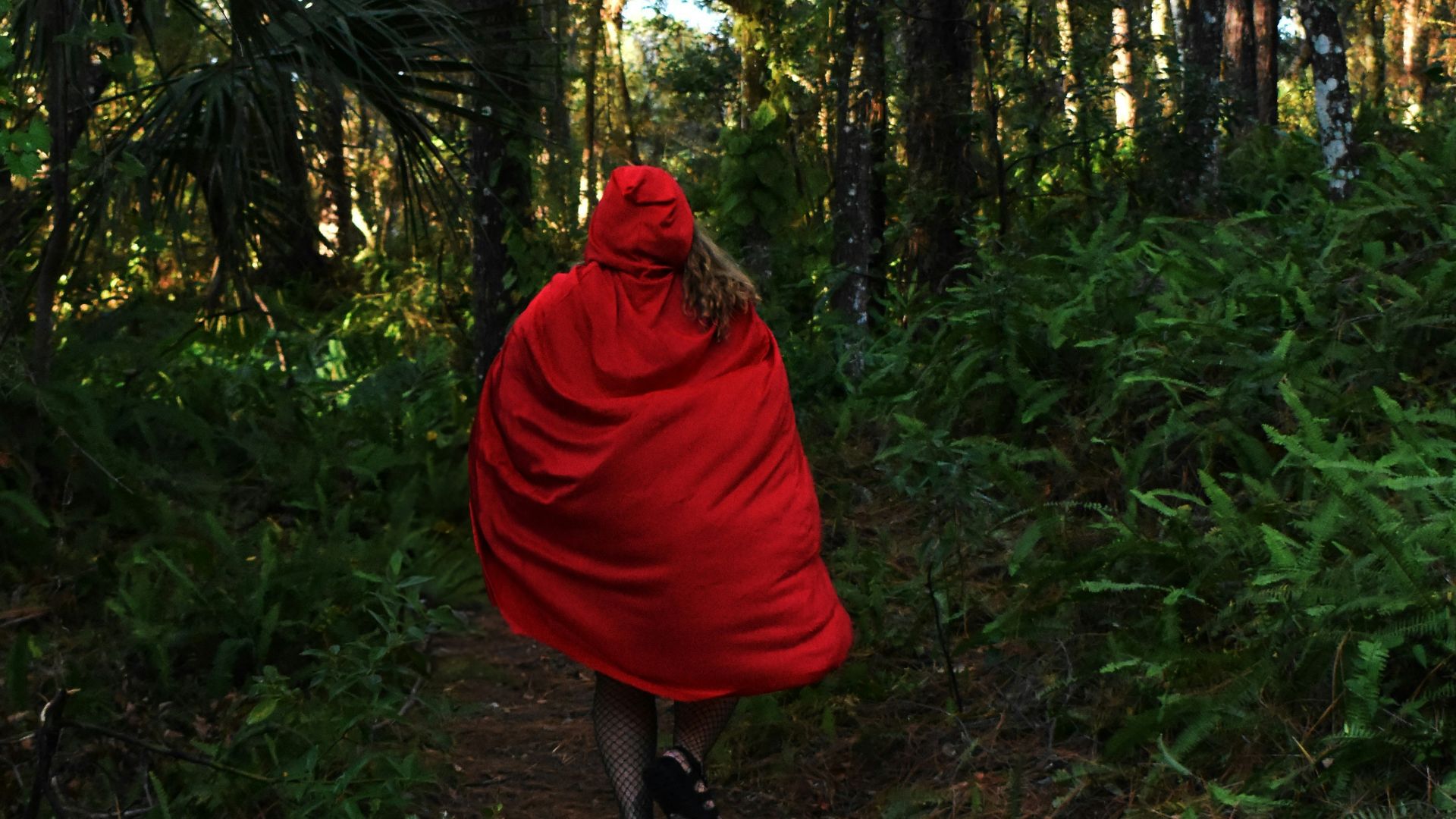 a woman in a red cape is walking through the woods