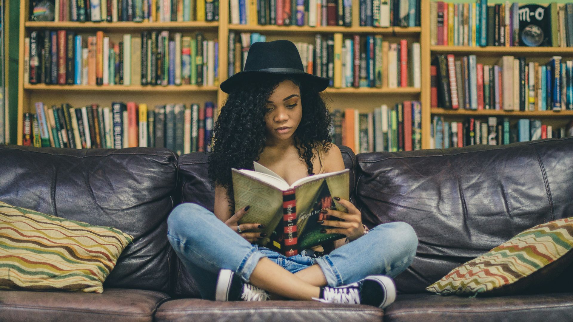 woman reading a book while sitting on black leather 3-seat couch