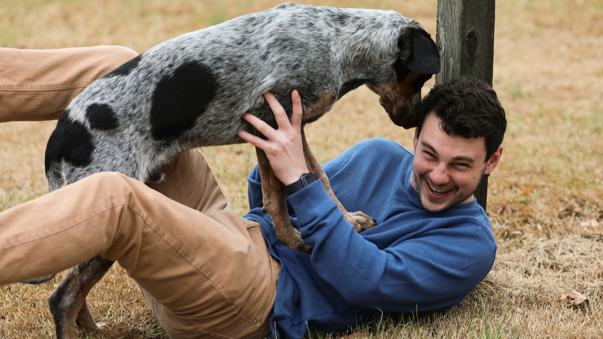 man in black jacket and brown pants holding black and white short coated dog
