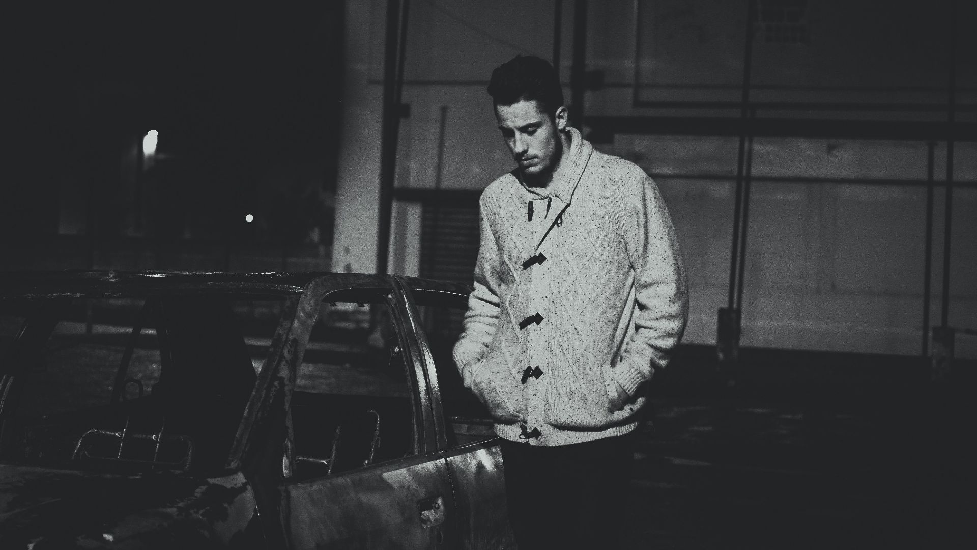 grayscale photo of man standing beside car