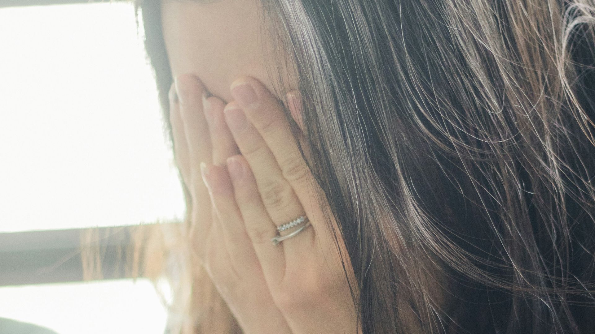 woman in brown shirt covering her face