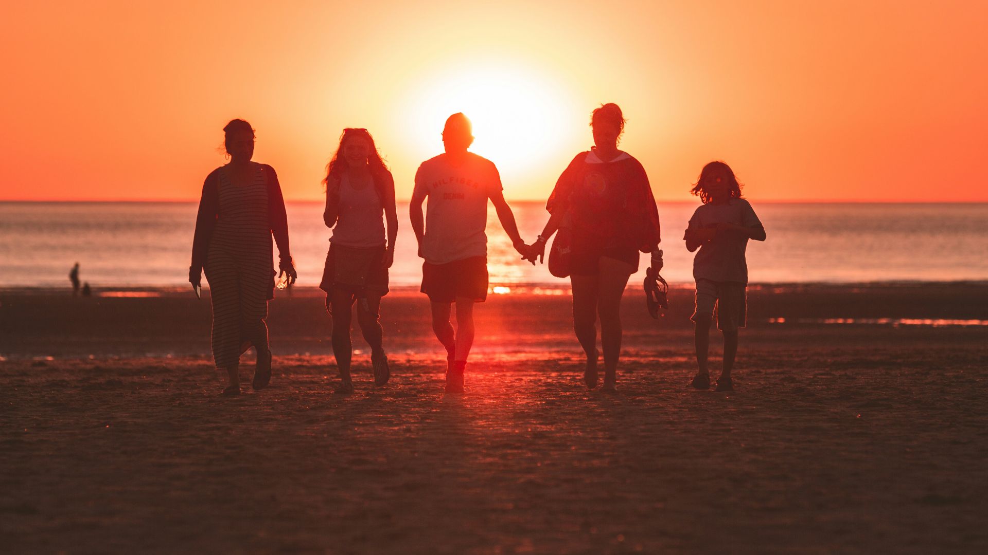 silhouette photo of five person walking on seashore during golden hour