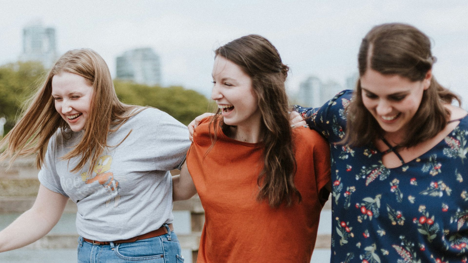 three women walking on brown wooden dock near high rise building during daytime