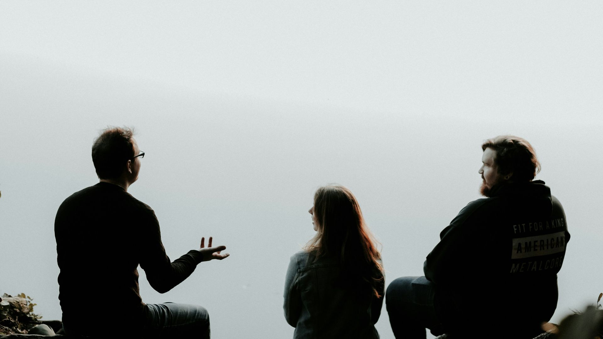 silhouette of three people sitting on cliff under foggy weather