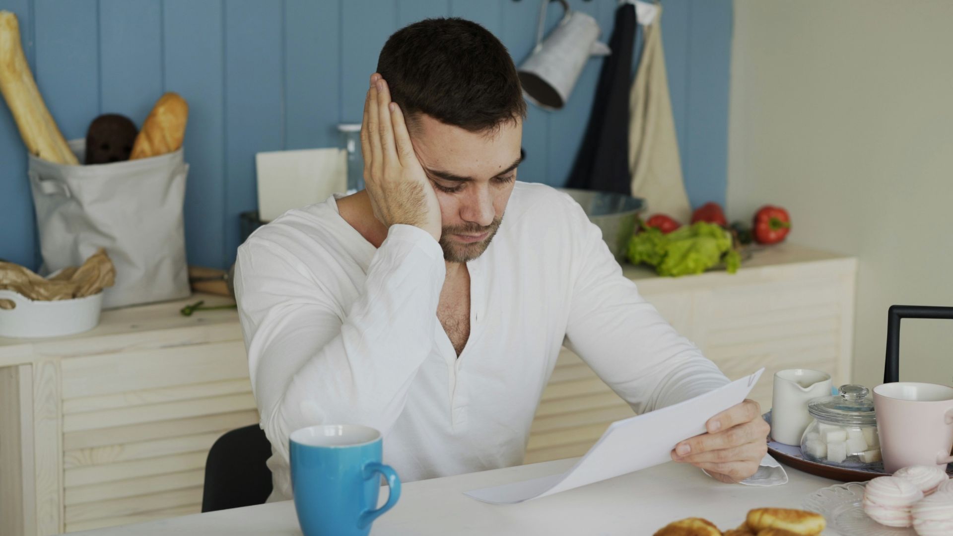 Man sitting at table reading papers with breakfast.