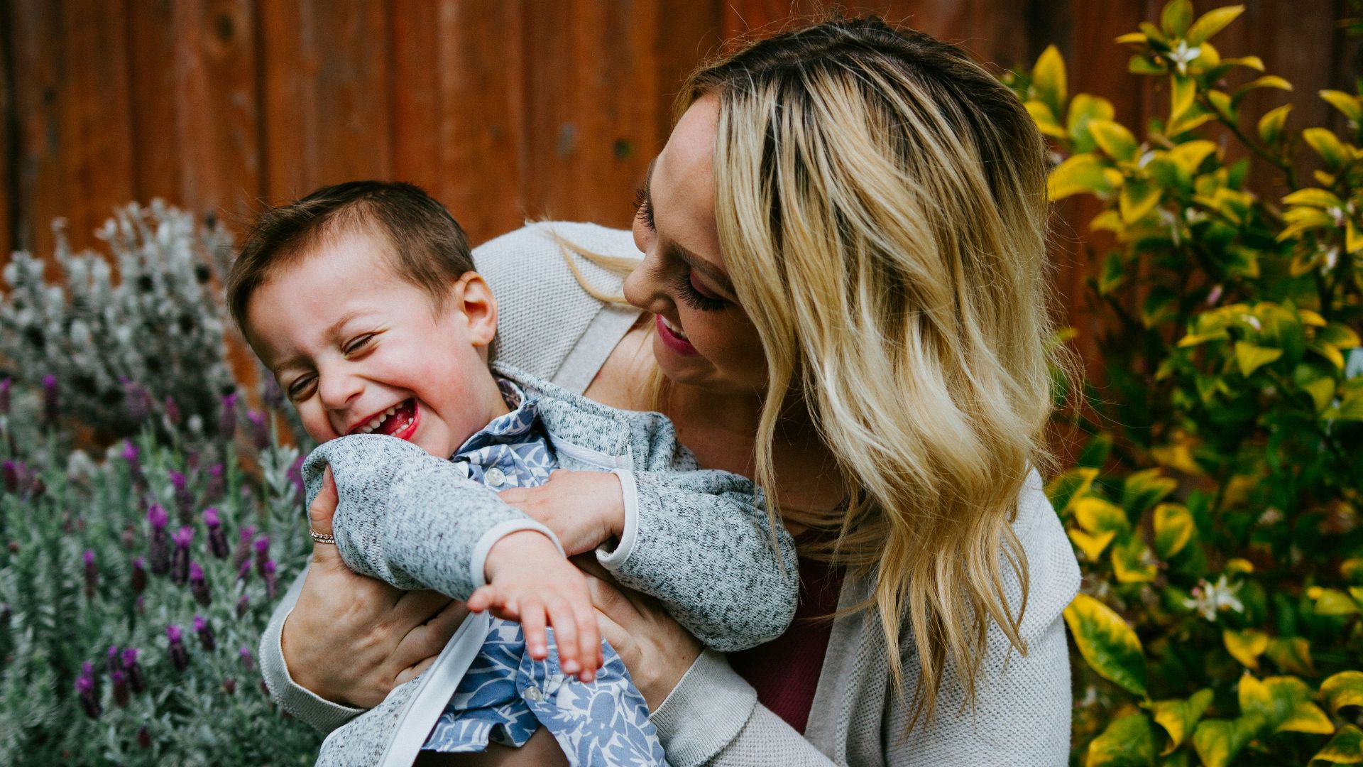 woman in gray sweater carrying baby in blue and white shirt