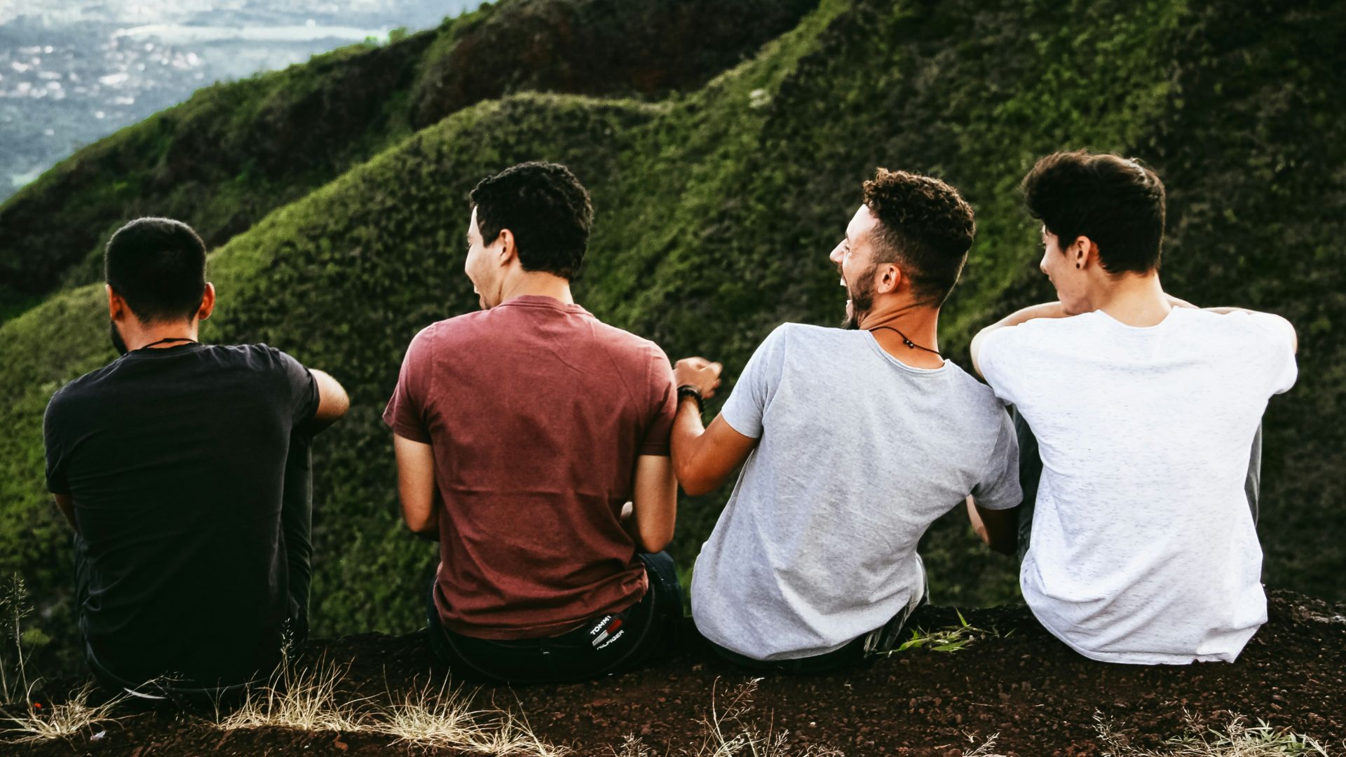 row of four men sitting on mountain trail