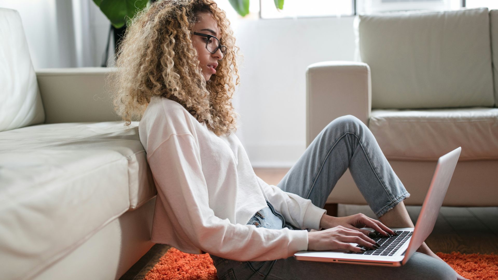 woman sitting on floor and leaning on couch using laptop