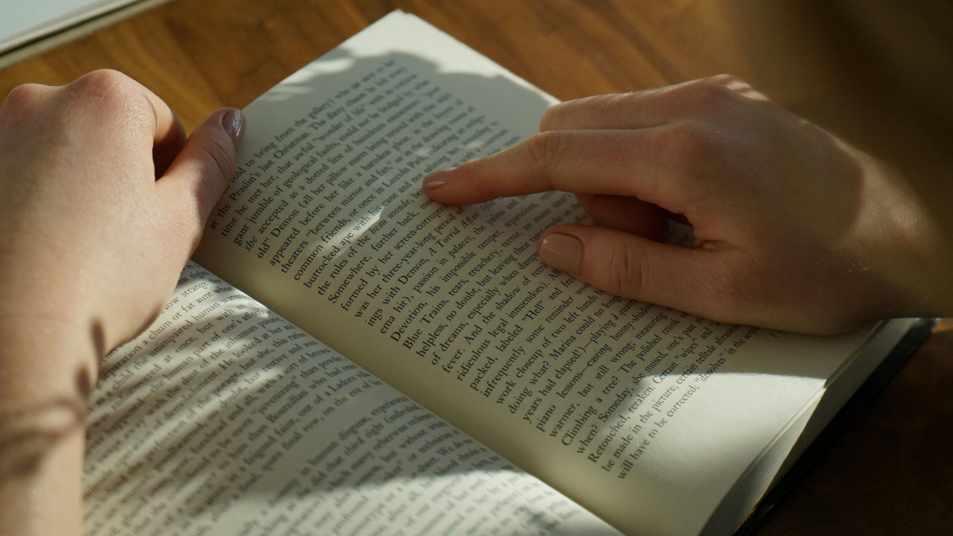 person reading book on brown wooden table taken at daytome