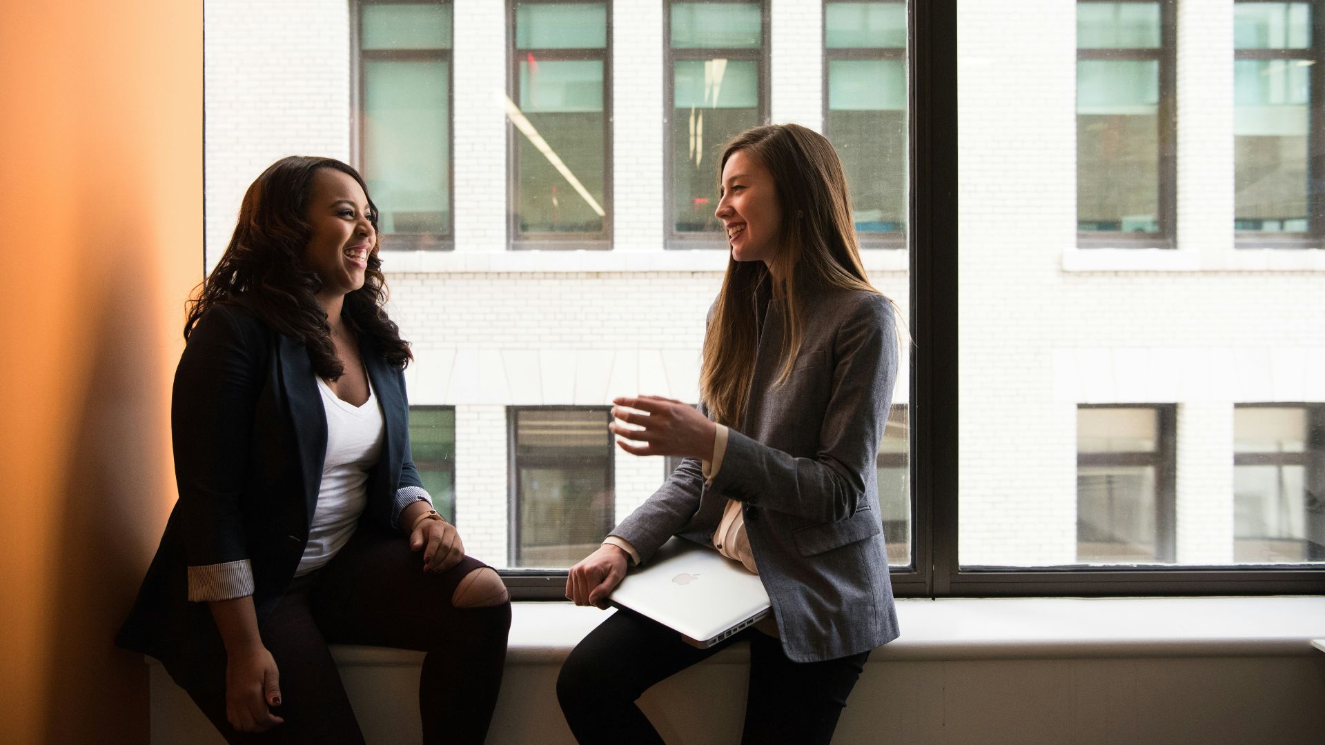 two woman sitting by the window laughing