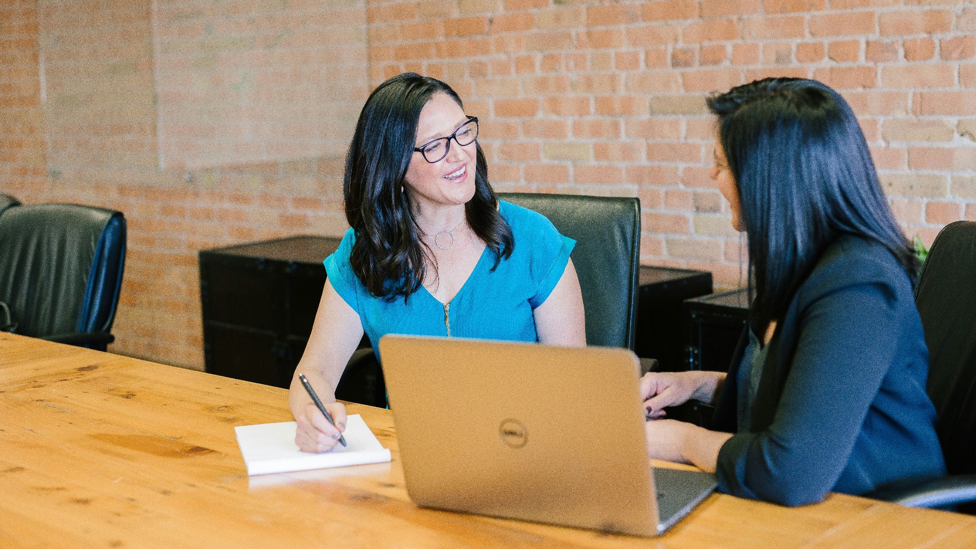 woman in teal t-shirt sitting beside woman in suit jacket