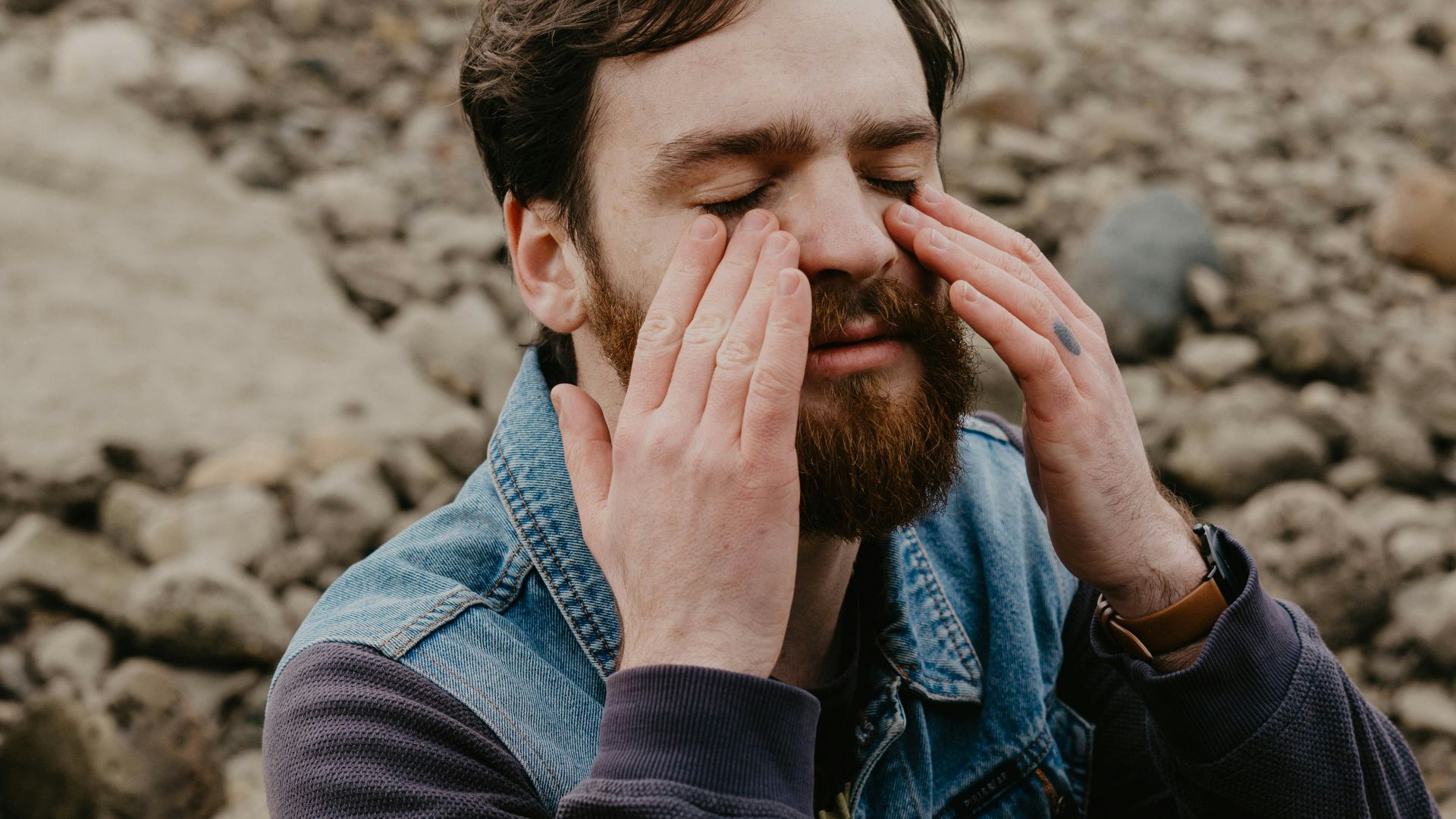 man in blue denim jacket covering his face with his hand