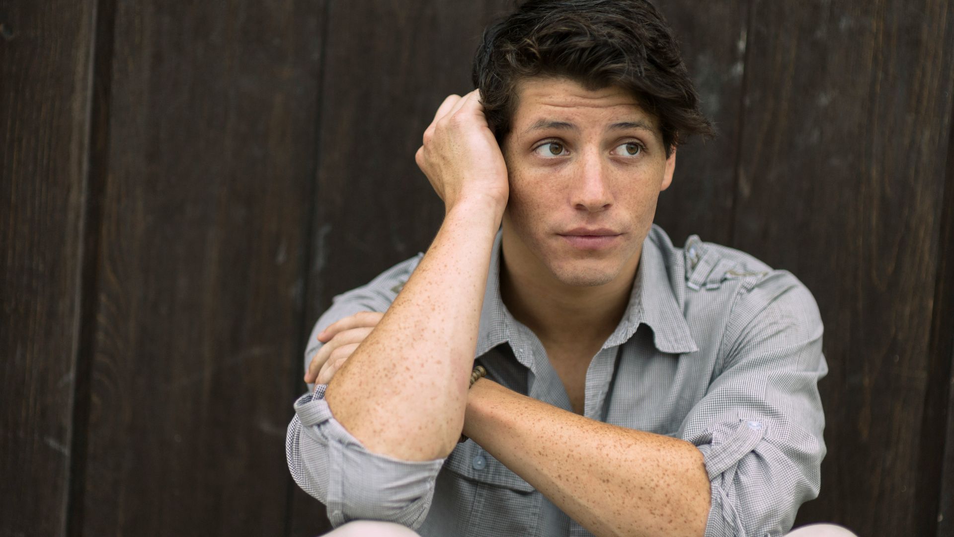 man wearing gray dress shirt leaning on brown wall