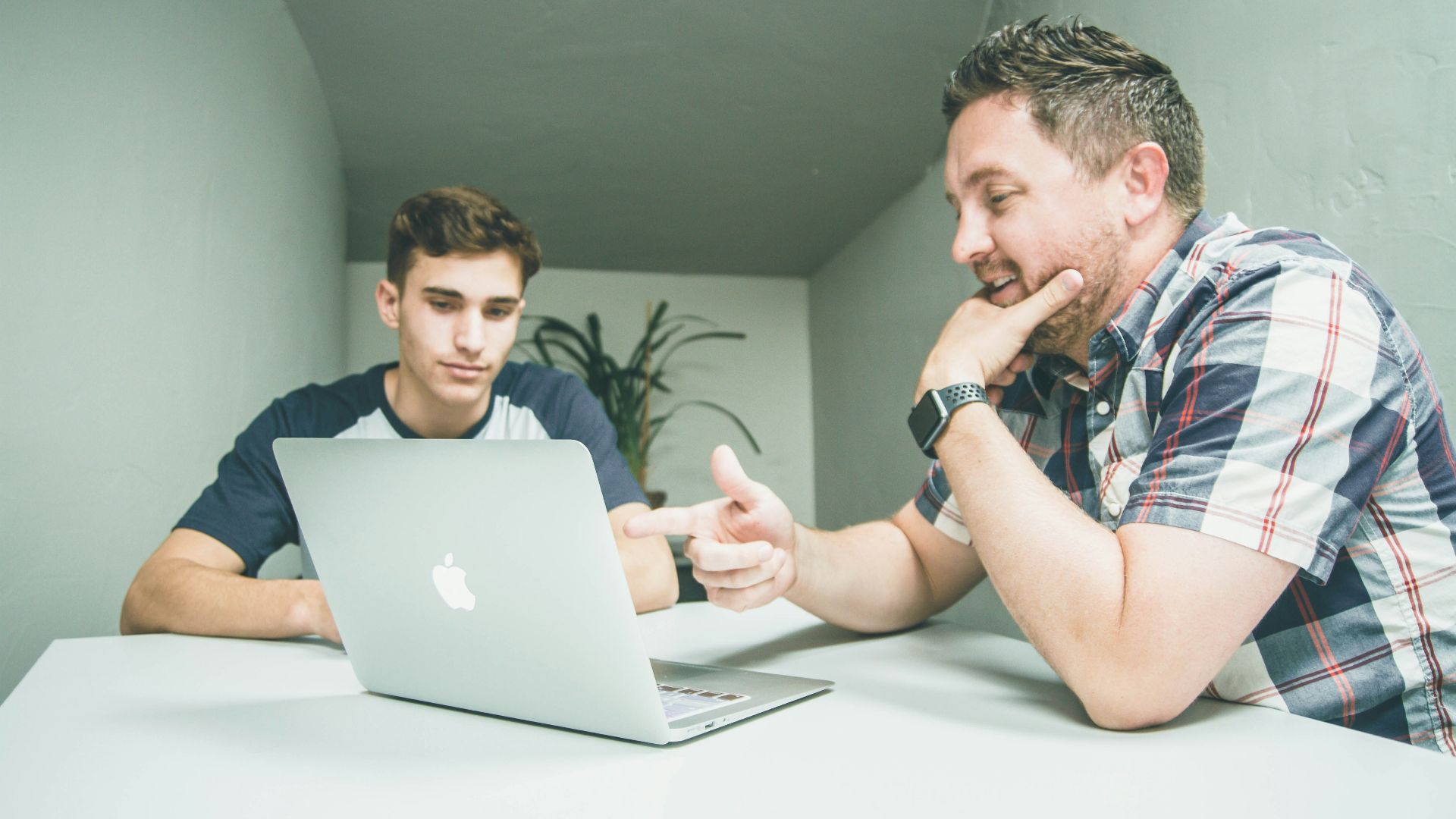 man wearing white and black plaid button-up sports shirt pointing the silver MacBook