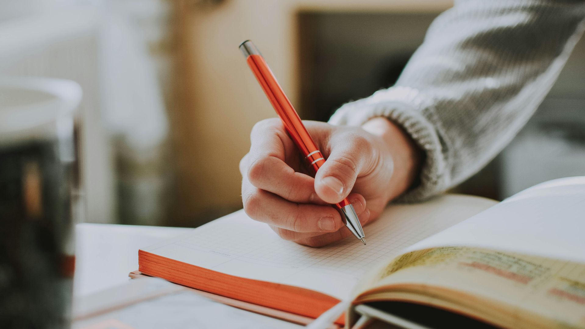person holding on red pen while writing on book