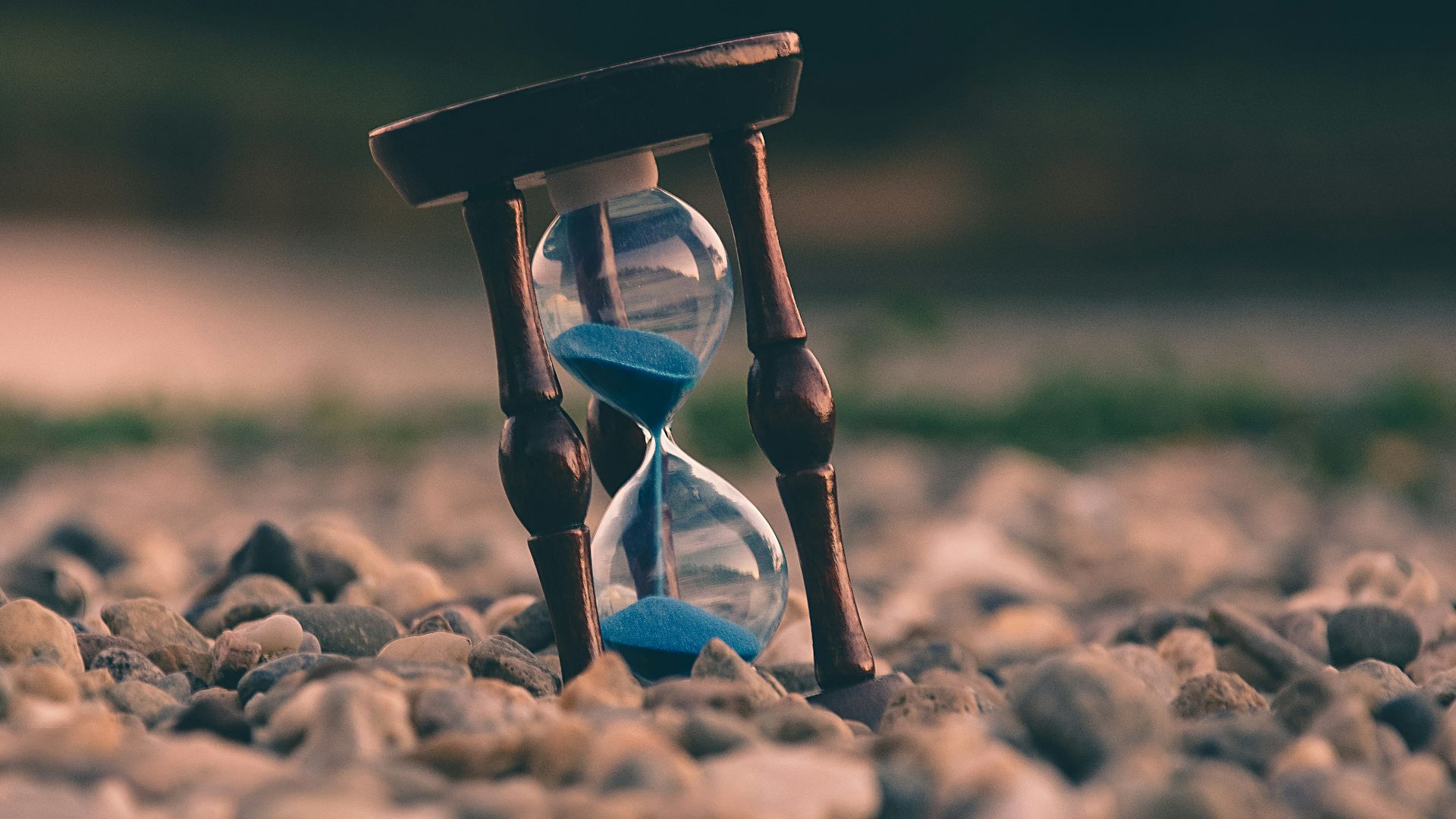 selective focus photo of brown and blue hourglass on stones