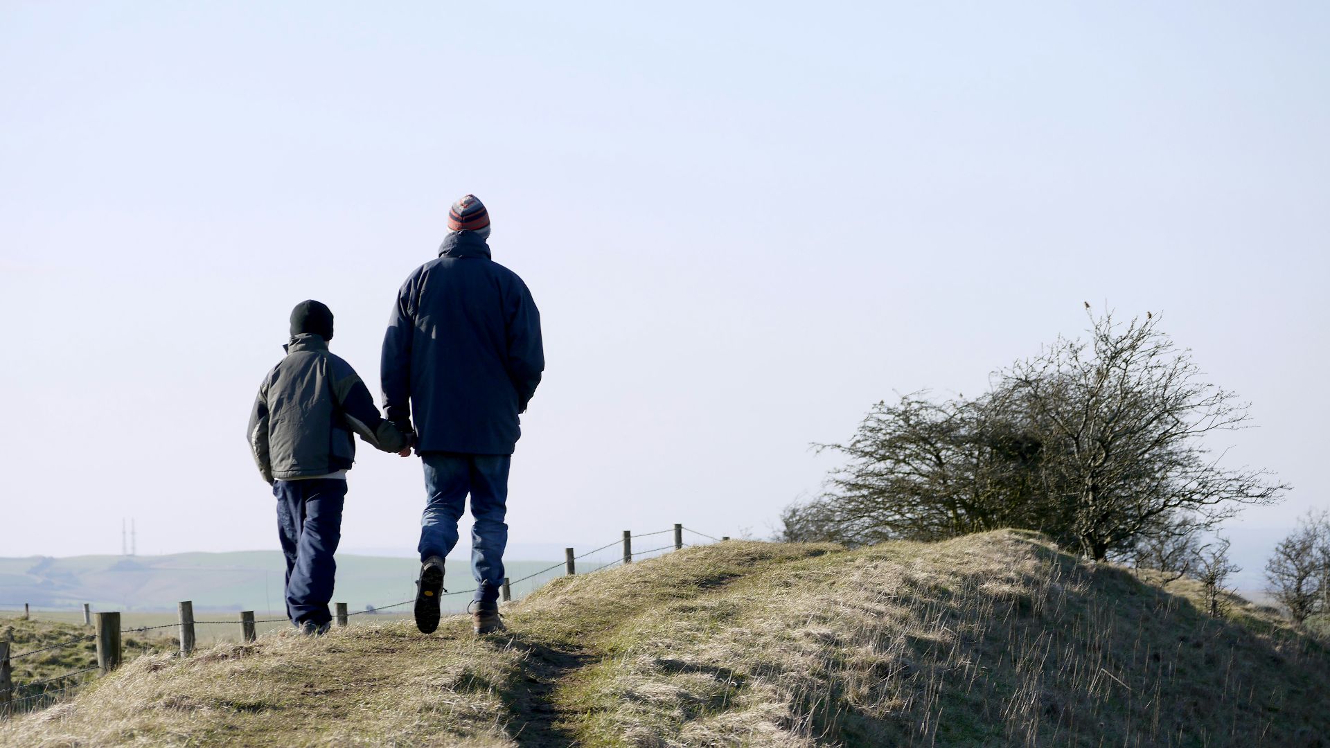 man and boy walking on grass near fence