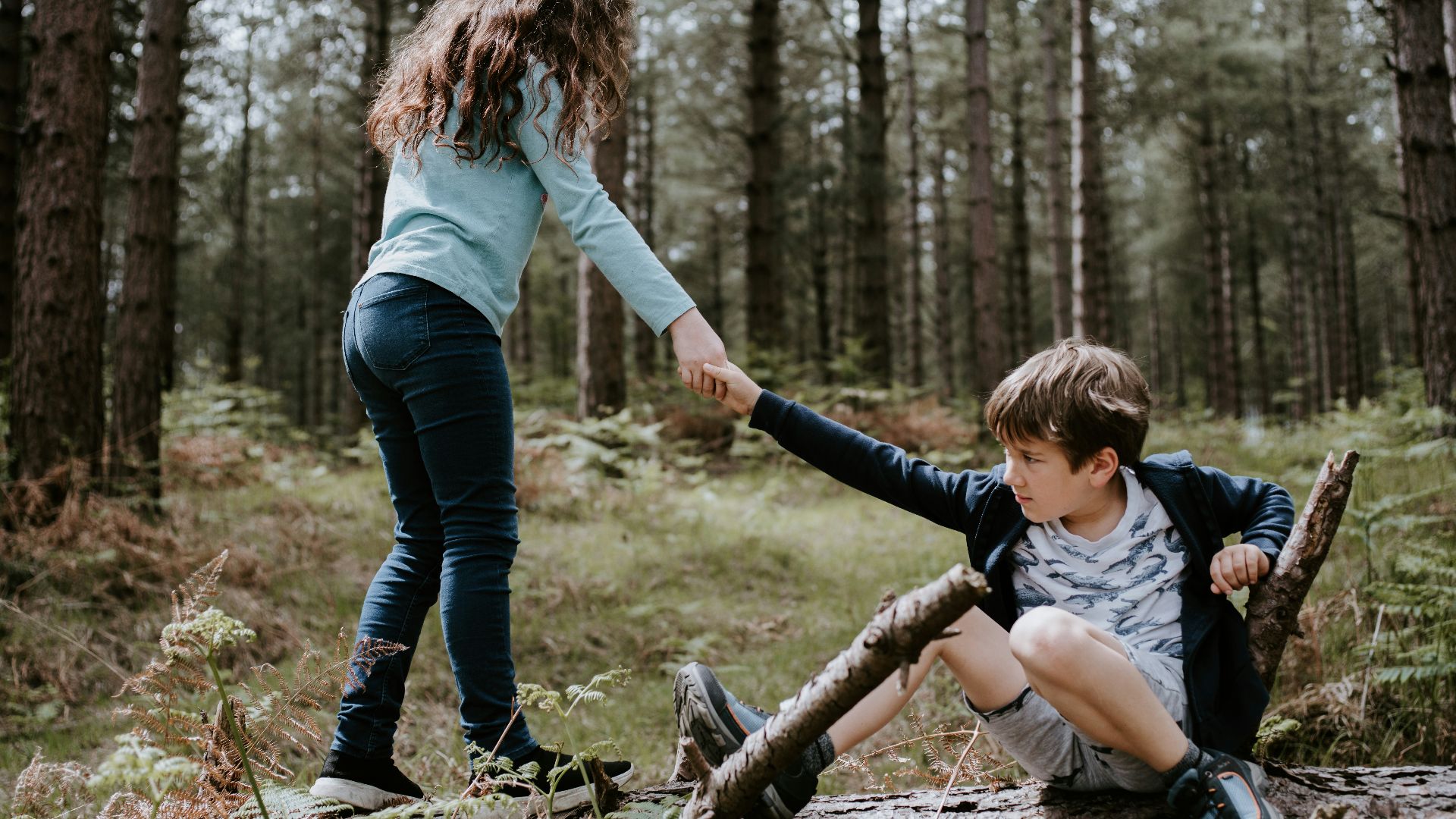 boy and girl playing on three tree log