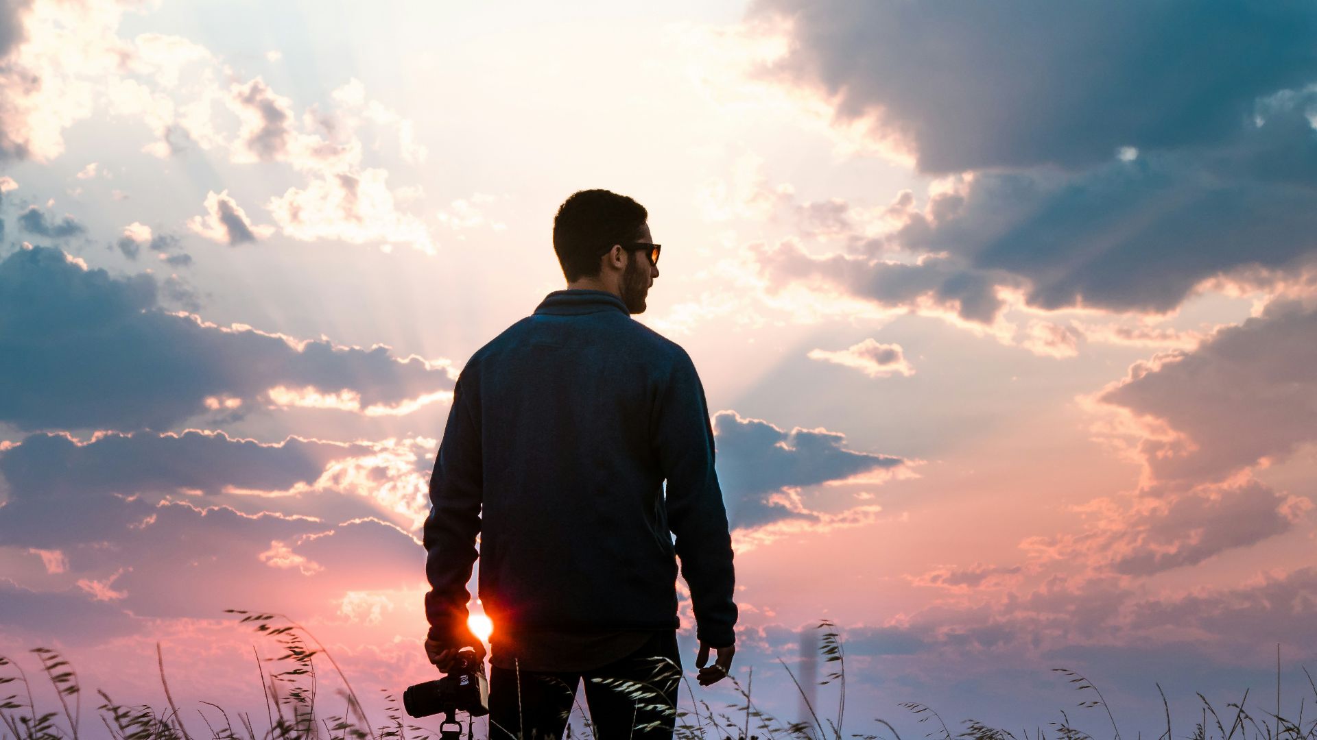 man in black long-sleeved shirt holding DSLR camera standing on grass