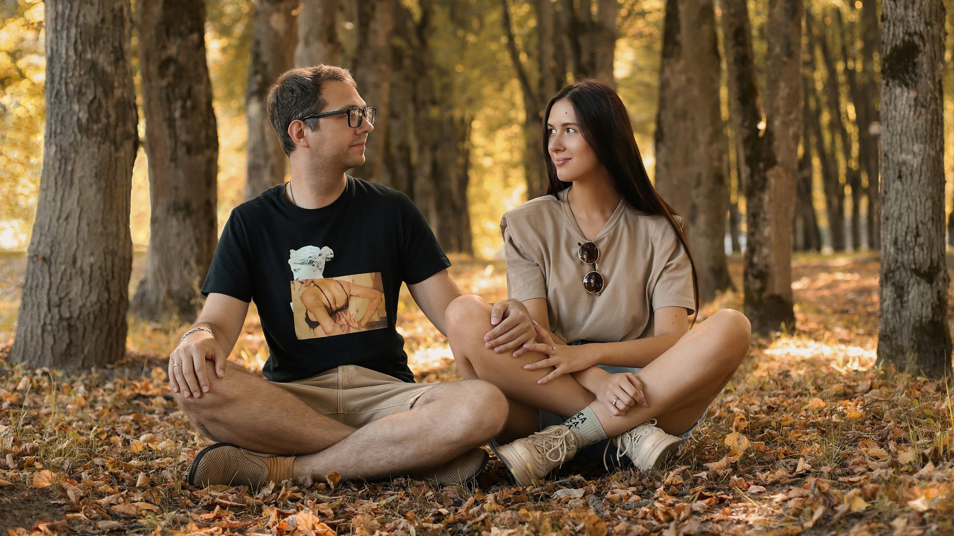 a man and a woman sitting on the ground in a forest