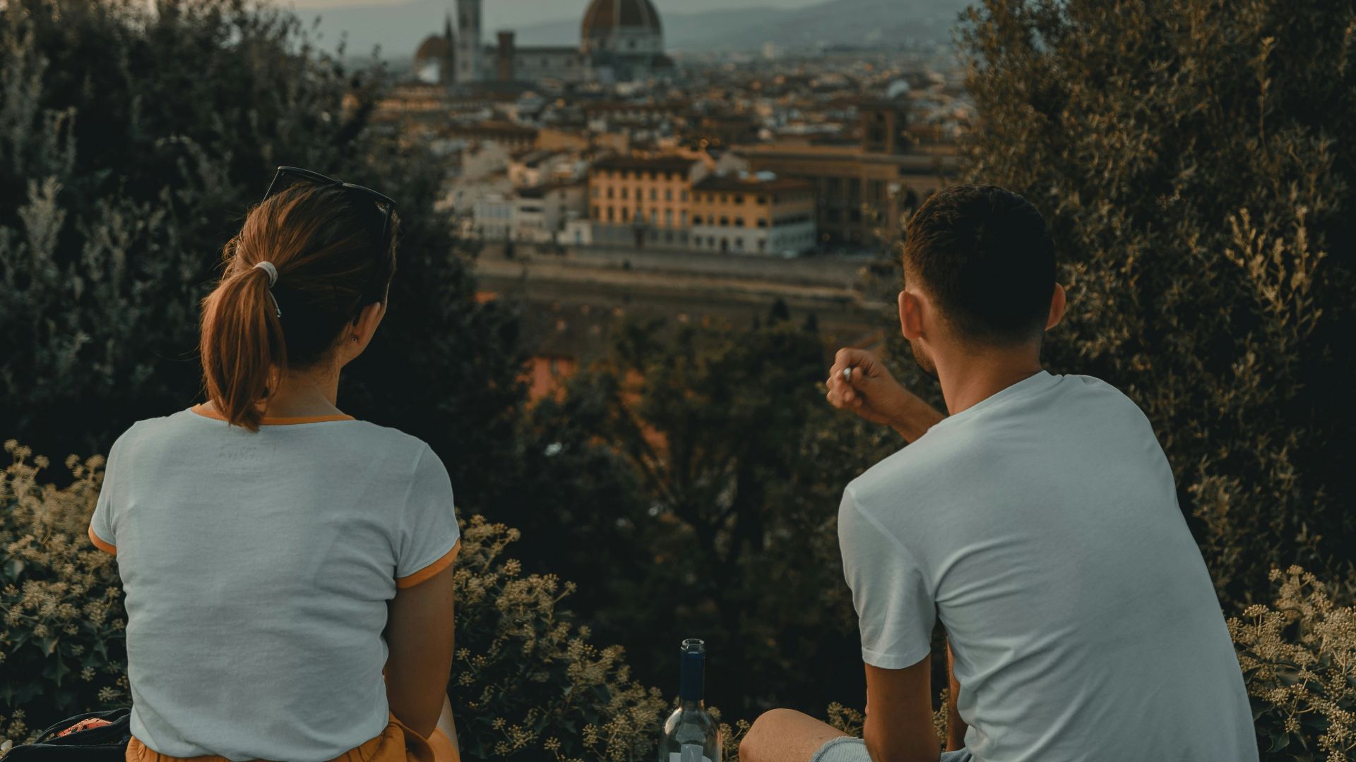 woman and man wearing white shirt while sitting near green trees during daytime