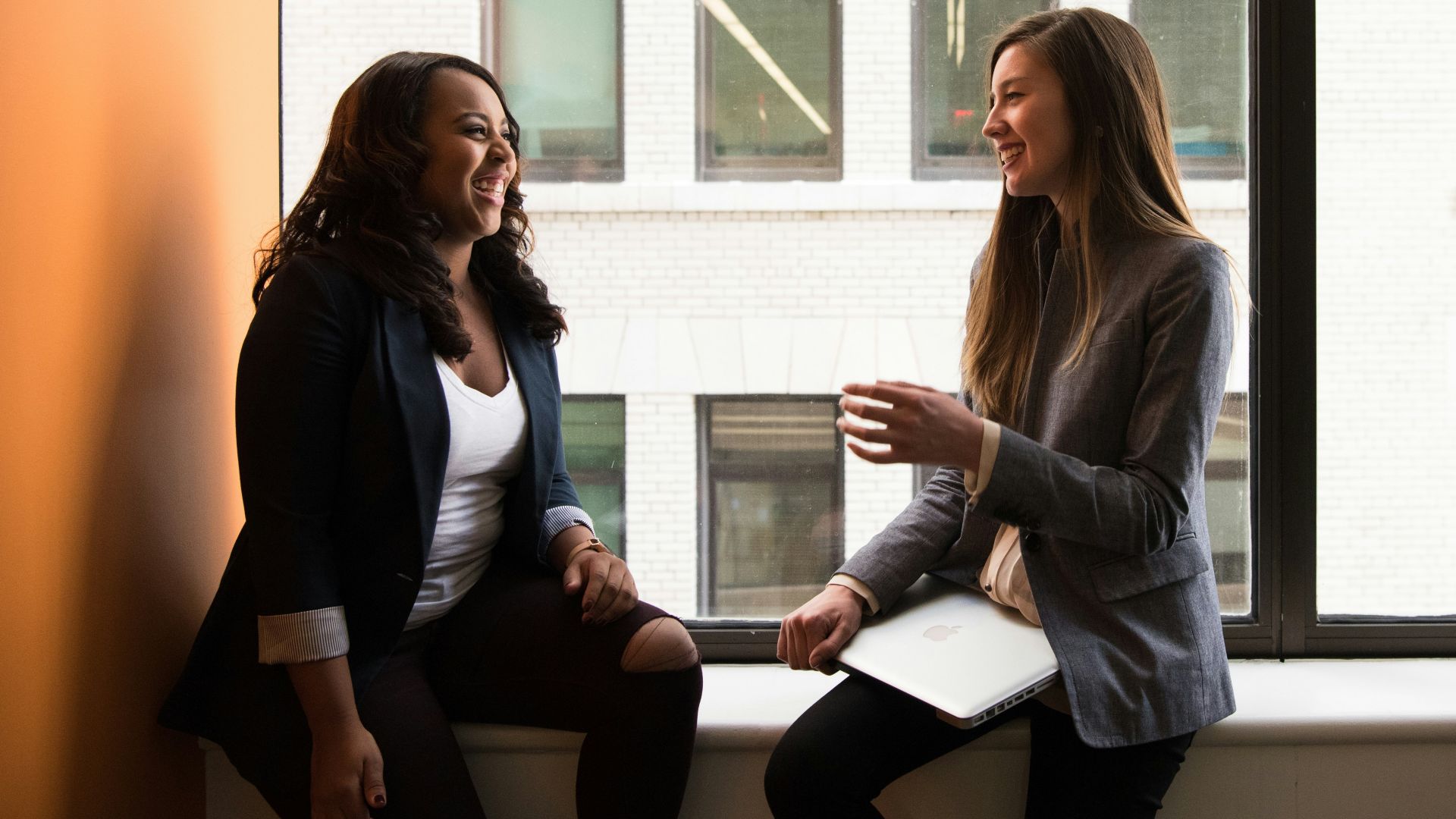 two woman sitting by the window laughing