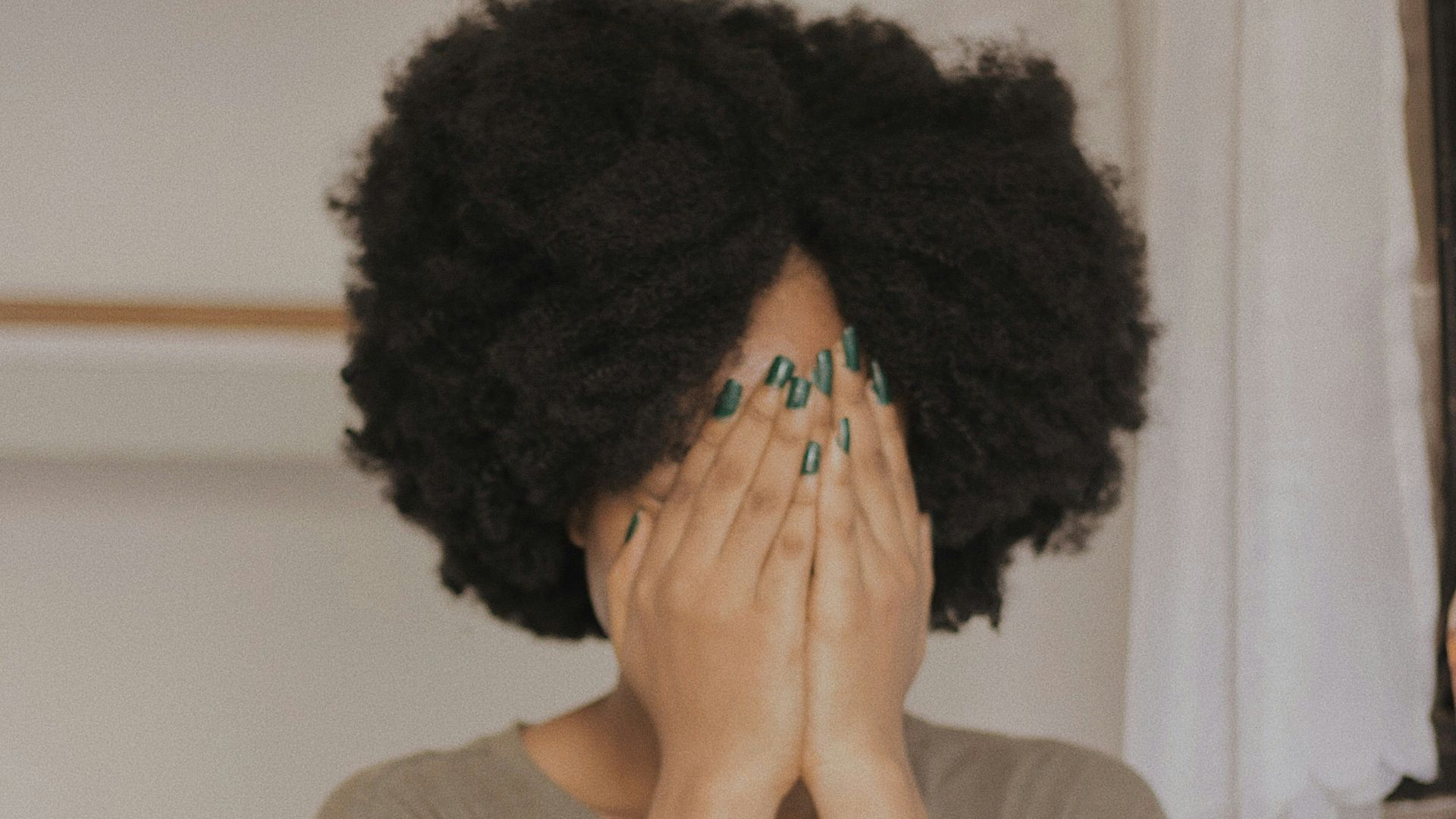 woman in gray t-shirt covering face with both hands