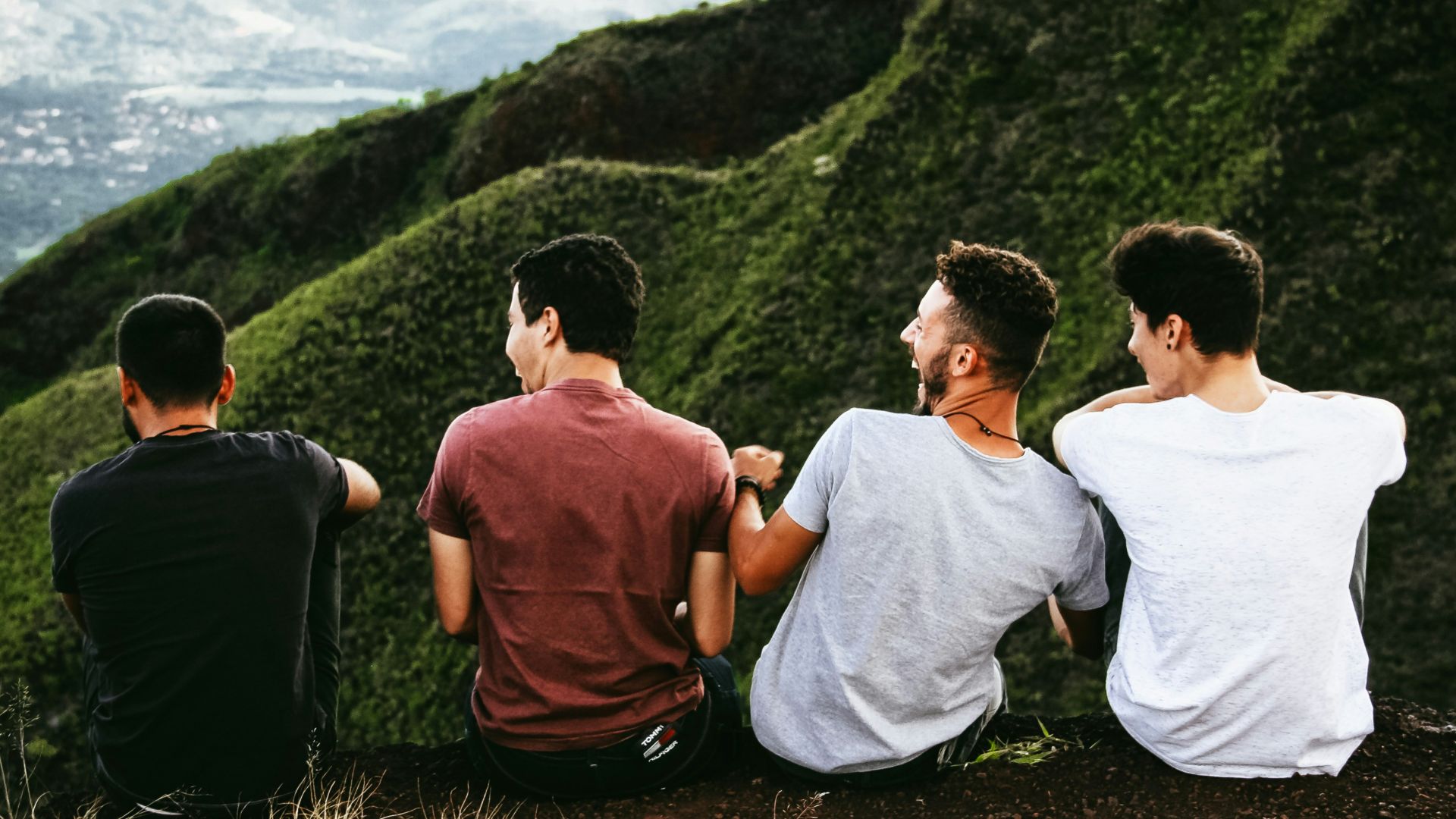 row of four men sitting on mountain trail