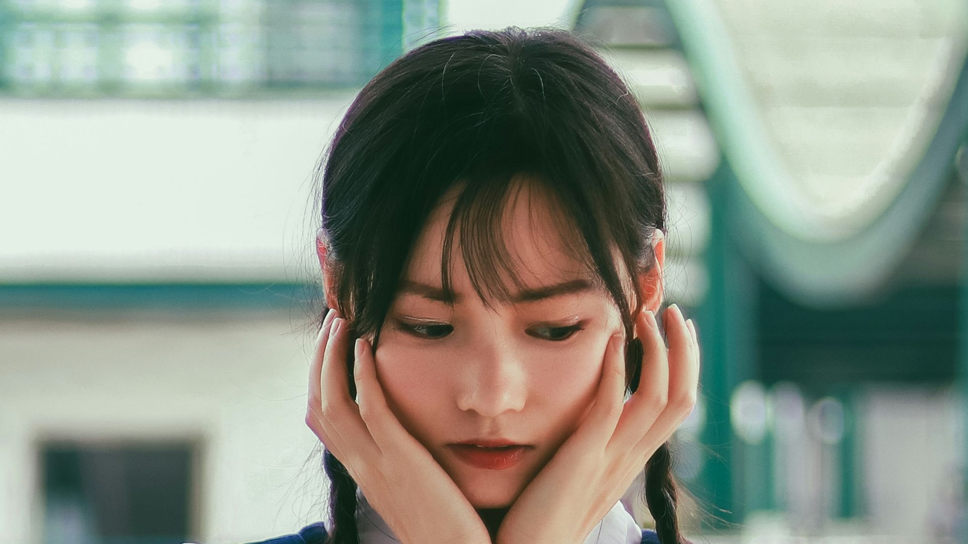 woman holding her face standing near white and green concrete building