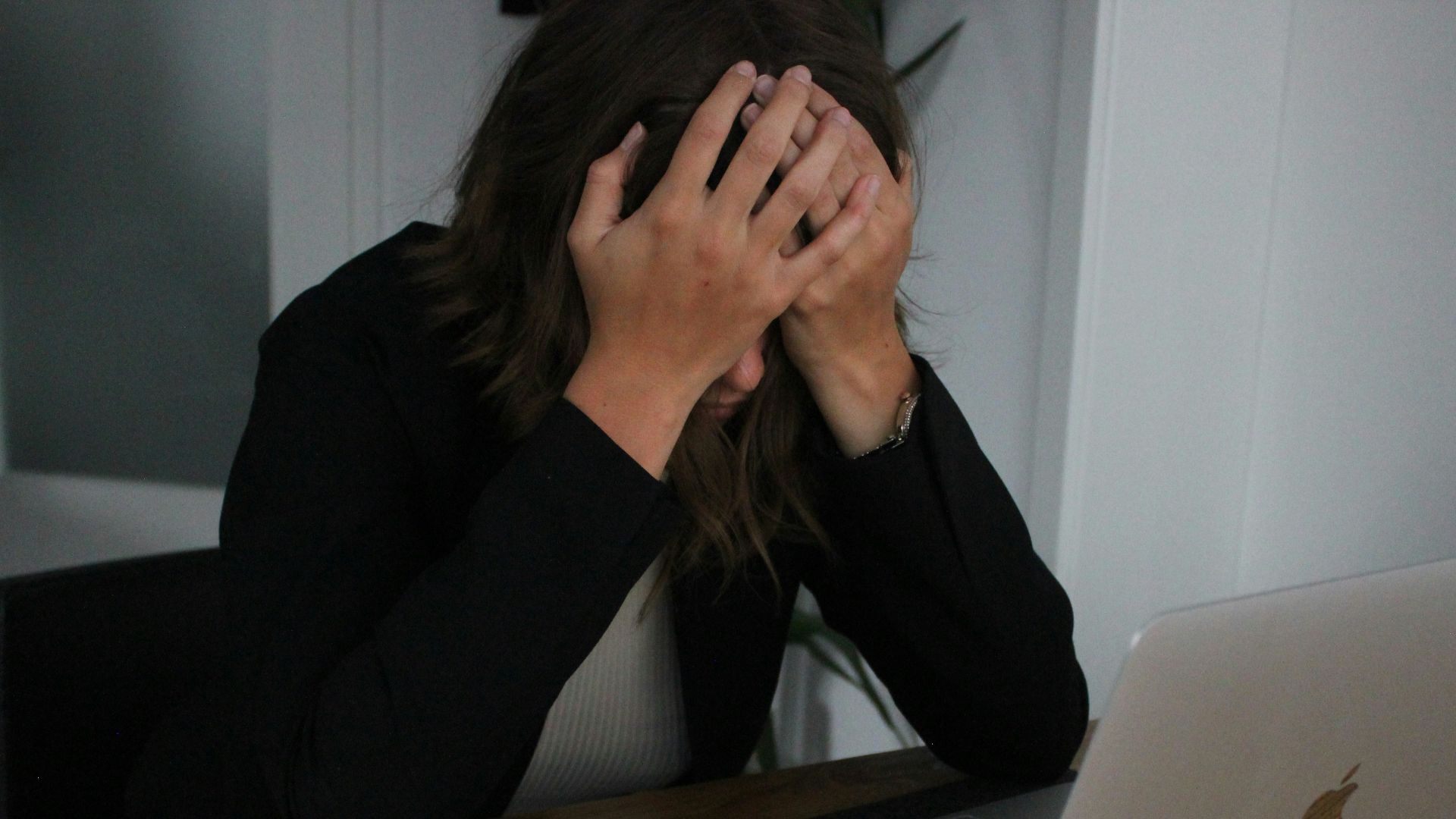 a woman covering her face while looking at a laptop