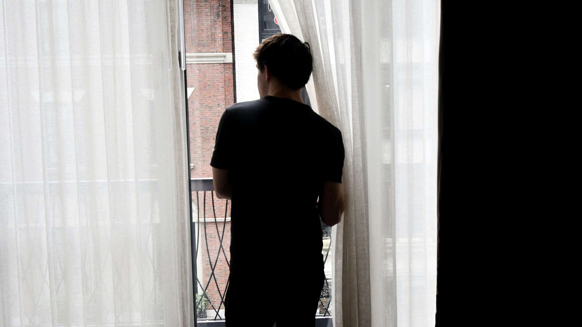 man in black crew neck t-shirt standing near white window curtain